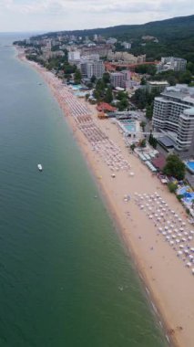 Kalabalık bir plajın renkli şemsiyeli ve denizde yüzen yüzücülerin canlı bir yaz gününün özünü yakaladığı görüntüler. Seyahat, turizm ve plaj yaşam tarzı promosyonu için mükemmel. Altın kumlar