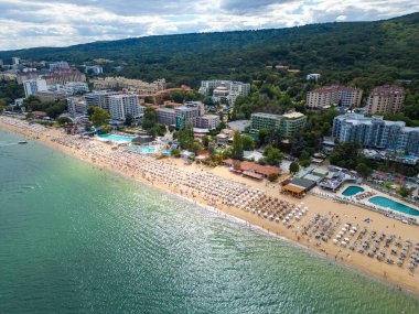 Deniz kenarında güneşli bir günün tadını çıkaran şemsiyelerle dolu güzel bir sahil manzarası. Yaz tatillerini, sahil tatil beldelerini ve seyahat deneyimlerini desteklemek için ideal. Altın kumlar