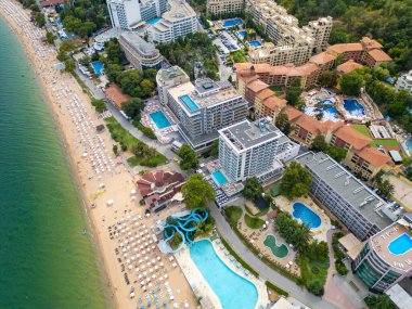 Deniz kenarında güneşli bir günün tadını çıkaran şemsiyelerle dolu güzel bir sahil manzarası. Yaz tatillerini, sahil tatil beldelerini ve seyahat deneyimlerini desteklemek için ideal. Altın kumlar