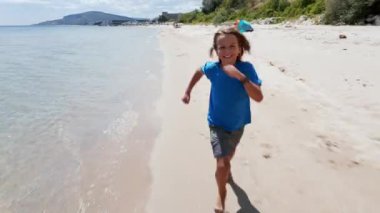 Sahilde koşuşturan neşeli çocuk kaygısız yaz günlerinin özünü yakalıyor. Parlak gülümseme ve kumlu kıyı şeridi özgürlük ve mutluluk hissi uyandırıyor..