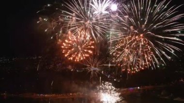 Muhteşem havai fişekler, gece gökyüzünü canlı bir şehrin rıhtımında aydınlatıyor, suyun altında yansımalar parıldıyor. Kutlamalar ve şenlik için mükemmel. Videoyu tersine çevir.