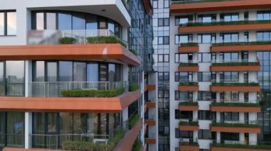 Hava aracı, canlı turuncu aksanlı ve yeşil balkonlu modern apartman binalarının cephelerini gösterirken kentsel mimariyi ve çağdaş yaşamı ön plana çıkarıyor..
