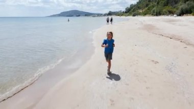Sahilde koşuşturan neşeli çocuk kaygısız yaz günlerinin özünü yakalıyor. Parlak gülümseme ve kumlu kıyı şeridi özgürlük ve mutluluk hissi uyandırıyor..
