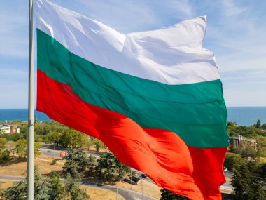 Bulgar bayrağı, arka planında engin deniz ve yeşil manzarayla bir kıyı kenti üzerinde gururla dalgalanıyor. Ulusal gurur ve güzel doğal manzaranın sembolü..