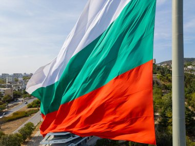 Bulgar bayrağı, arka planında engin deniz ve yeşil manzarayla bir kıyı kenti üzerinde gururla dalgalanıyor. Ulusal gurur ve güzel doğal manzaranın sembolü..