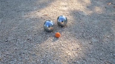 Petanque toplarına yakın çekim ve oyun sırasında çakıl üzerinde küçük bir hedef topu. Parlak metal toplar güneş ışığını yansıtıyor ve bu açık hava sporunun özünü yansıtıyor..