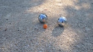 Petanque toplarına yakın çekim ve oyun sırasında çakıl üzerinde küçük bir hedef topu. Parlak metal toplar güneş ışığını yansıtıyor ve bu açık hava sporunun özünü yansıtıyor..