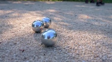 Petanque toplarına yakın çekim ve oyun sırasında çakıl üzerinde küçük bir hedef topu. Parlak metal toplar güneş ışığını yansıtıyor ve bu açık hava sporunun özünü yansıtıyor..