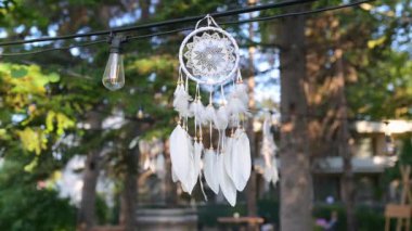 Güneş ışığı beyaz tüylü narin bir düş kapanı aracılığıyla parlıyor, dışarıda asılı duruyor. Boho temalı tasarımlar, doğa geçmişi ve barışçıl dekorasyon kavramları için mükemmel..