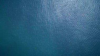 Sakin, derin mavi okyanus suyunun havadan görünüşü hafif dalgalanmalar ve doğal güneş ışığı yansımaları. Arkaplan dokuları, doğa temaları veya sakin deniz manzaraları için ideal.