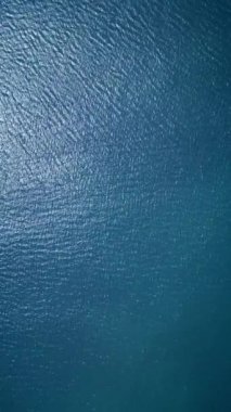 Sakin, derin mavi okyanus suyunun havadan görünüşü hafif dalgalanmalar ve doğal güneş ışığı yansımaları. Arkaplan dokuları, doğa temaları veya sakin deniz manzaraları için ideal.
