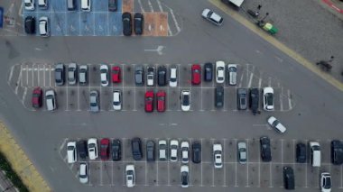 Kalabalık bir otoparkta sayısız araç işaretli yerleri işgal ediyor, parlak gün ışığı altında bir şehirde çeşitli renk ve stillerin karışımını sergiliyor.