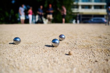 Petanque toplarının yakın çekimleri çakıllara saçılmış ve hedef top hedefte. Parlak metal toplar güneş ışığını yansıtıyor. Parktaki açık havada eğlenceli bir anı yakalıyor..