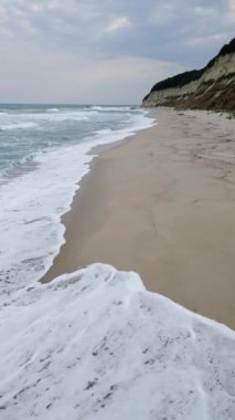 Turkuaz dalgaların engebeli kayalıklarla çevrili kumlu bir sahile yavaşça vurduğu sakin bir sahil sahnesi. Doğa, seyahat ya da deniz manzarası teması için mükemmel.