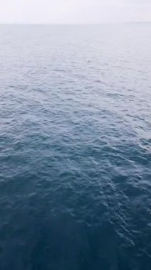 Sakin bir okyanus yüzeyi, berrak gökyüzünün altındaki güneş ışığını yansıtır ve suyun sakinliğini vurgular. Sahne öğle vakti huzur ve dinginlik hissi veriyor..
