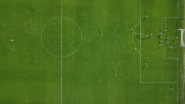 Yukarıdan aşağıya bir futbol maçının insansız hava aracı görüntüleri, kaleye yakın yoğun bir oyunda sahadaki oyuncuları gösteriyor ve benzersiz bir hava perspektifi sunuyor..