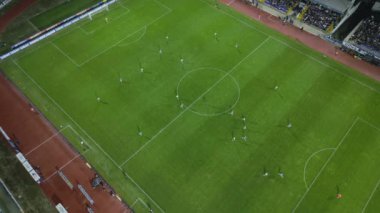 Yukarıdan aşağıya bir futbol maçının insansız hava aracı görüntüleri, kaleye yakın yoğun bir oyunda sahadaki oyuncuları gösteriyor ve benzersiz bir hava perspektifi sunuyor..