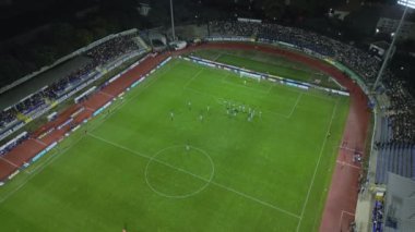 Yukarıdan aşağıya bir futbol maçının insansız hava aracı görüntüleri, kaleye yakın yoğun bir oyunda sahadaki oyuncuları gösteriyor ve benzersiz bir hava perspektifi sunuyor..