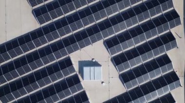 Büyük bir dizi güneş paneli ticari bir binanın çatısını kaplayarak enerji için güneş ışığını yakalıyor. Kurulum, kentsel bir ortamda sürdürülebilir uygulamaları vurguluyor.