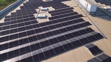 Büyük bir dizi güneş paneli ticari bir binanın çatısını kaplayarak enerji için güneş ışığını yakalıyor. Kurulum, kentsel bir ortamda sürdürülebilir uygulamaları vurguluyor.