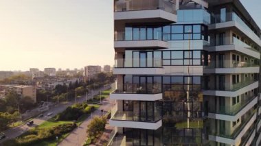 Çağdaş bir konut binasında geniş cam elementler bulunur. Güneş ufukta batarken hareketli şehir yaşamını yansıtır ve sıcak bir ışık yayar..