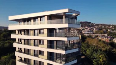 Çağdaş bir konut binasında çarpıcı, kıvrımlı cephesi ve büyük cam balkonları sergileniyor. Batan güneşin yumuşak ışığını resimli bir banliyö arka planına yansıtıyor..