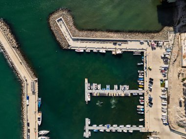 Bir marinaya çok sayıda tekne yanaşmış ve bazıları uzun bir rıhtım boyunca demirlemiş. Su sakin, ve güneş gölgeleri salıyor, canlı sahneyi güçlendiriyor..