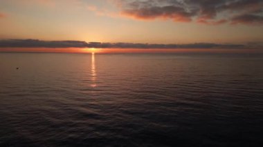 Sakin okyanus suları üzerinde sersemletici bir gün doğumunun sakin bir görüntüsü. Huzurlu bir ufuk ve sıcak altın tonlarını yansıtan ince bulutlar..