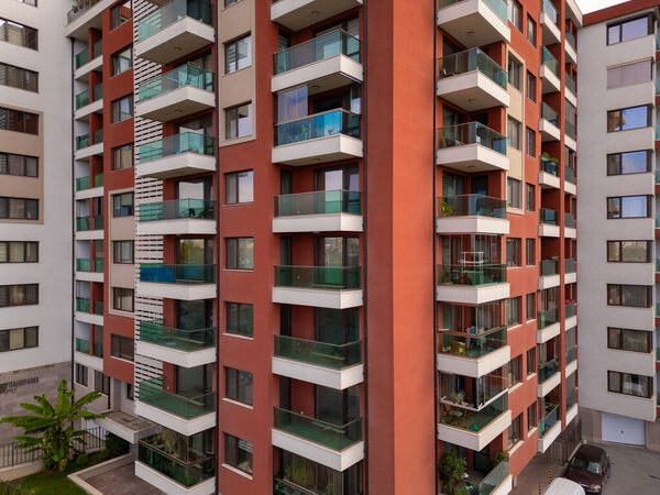 Современное жилое здание, захваченное беспилотником, подчеркивает его красочный фасад, стеклянные балконы и городскую жилую архитектуру с чистым, современным дизайном.