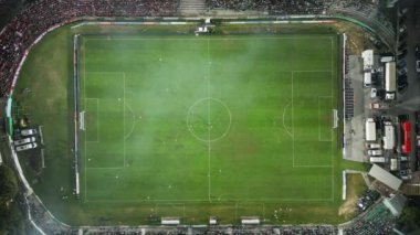 Yukarıdan aşağıya bir futbol maçının insansız hava aracı görüntüleri, kaleye yakın yoğun bir oyunda sahadaki oyuncuları gösteriyor ve benzersiz bir hava perspektifi sunuyor..