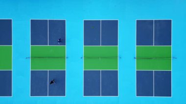 Mavi ve yeşil yüzeylerin renkli, geometrik desenlerini ve dinamik atletik hareketlerini gözler önüne seren canlı picleball sahalarının hava drone çekimi..