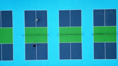 Mavi ve yeşil yüzeylerin renkli, geometrik desenlerini ve dinamik atletik hareketlerini gözler önüne seren canlı picleball sahalarının hava drone çekimi..