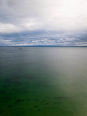 Uçsuz bucaksız bir okyanusun dramatik, bulutlu bir gökyüzü altında panoramik bir görüntüsü. Ufuktaki uzak bir gemi izolasyon ve uçsuz bucaksızlık hissini arttırır. Deniz manzarası ve deniz teması için ideal.