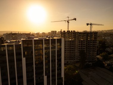 Gün batımında gökdelen bir binanın inşaat alanını kaydeden bir drone videosu. Yapılar, beton iskelet, vinç ve iskele sıcak güneş ışığıyla yıkanarak kentsel gelişimi vurguluyor.