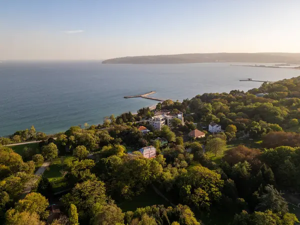 Modern binalar, yemyeşil alanlar ve arka planda sakin mavi deniz olan deniz manzaralı bir deniz manzarası. Altın saat ışığı huzurlu şehir ve kıyı manzarasını güçlendiriyor..