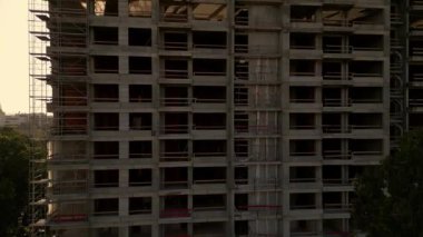 Gün batımında gökdelen bir binanın inşaat alanını kaydeden bir drone videosu. Yapılar, beton iskelet, vinç ve iskele sıcak güneş ışığıyla yıkanarak kentsel gelişimi vurguluyor.
