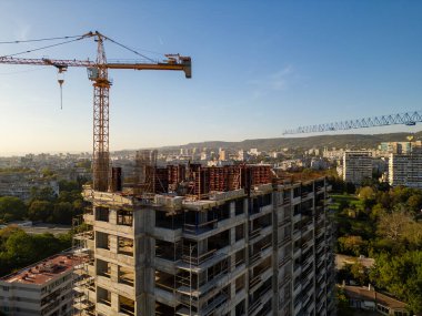 Gün batımında gökdelen bir binanın inşaat alanını kaydeden bir drone videosu. Yapılar, beton iskelet, vinç ve iskele sıcak güneş ışığıyla yıkanarak kentsel gelişimi vurguluyor.