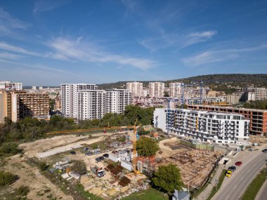 Bir vinç ve yakınlardaki konut binaları olan bir inşaat alanının insansız hava aracı videosu. Görüntüler yeşil ve şehir hayatı ile çevrili kentsel gelişimin ilerlemesini yakalıyor..