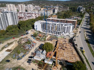 Bir vinç ve yakınlardaki konut binaları olan bir inşaat alanının insansız hava aracı videosu. Görüntüler yeşil ve şehir hayatı ile çevrili kentsel gelişimin ilerlemesini yakalıyor..