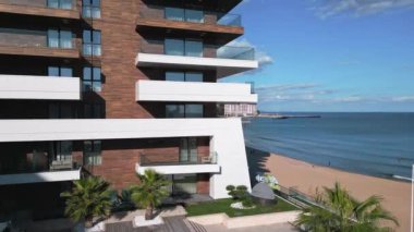 Camdan balkonları olan modern bir deniz manzaralı apartman dairesi. Dağınık bulutlu mavi gökyüzü huzur veren kıyı şeridine ekleniyor..