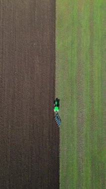 Yeşil bir traktörün tarlayı sürüşünün havadan görüntüsü yeşil otla yeni sürülmüş toprak arasında belirgin bir kontrastlık yaratıyor. Tarım makineleri tarım arazilerinde çalışıyor.