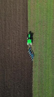 Yeşil bir traktörün tarlayı sürüşünün havadan görüntüsü yeşil otla yeni sürülmüş toprak arasında belirgin bir kontrastlık yaratıyor. Tarım makineleri tarım arazilerinde çalışıyor.
