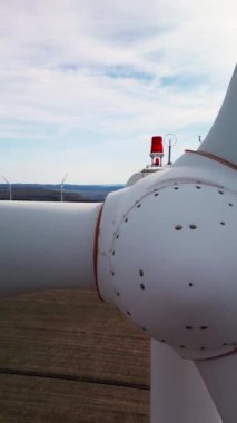 Kırmızı ışıklı bir rüzgar türbinine yakın plan, arka planda çeşitli türbinleri gösteriyor. Kırsal bölgedeki yenilenebilir enerji altyapısının havadan görüşü.