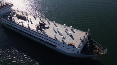 Sakin sularda seyreden büyük bir kargo gemisinin hava görüntüsü, deniz yüzeyine yansıyan güneş ışığı. Dinamik bir deniz sahnesi gemilerin yolculuğunu yakalıyor..