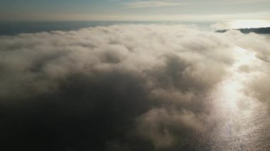 Okyanus üzerindeki yoğun sisin havadan görünüşü, sudan yansıyan güneş ışığı. Sahne, bulutlar ve ışık katmanlarıyla huzurlu ve mistik bir atmosfer yaratır..