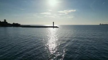 Gün batımında sakin bir denizdeki deniz fenerinin insansız hava aracı görüntüleri. Güneş suya yansıyor. Huzurlu deniz manzarası, kıyı manzarası, ufuk manzarası, sakin atmosfer, deniz manzarası..