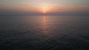 Gün batımında sakin bir denizin, yumuşak dalgalar ve ufukta süzülen ılık bir güneşin, rahatlatıcı ve pitoresk bir okyanus manzarası yaratarak, rahatlatıcı temalar için ideal bir hava aracı görüntüsü..