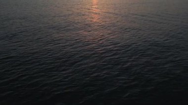 Sakin denizin üzerinde sakin bir gün batımının hava drone görüntüsü, yumuşak pastel renkler suya yansıyor, huzur verici ve sakin bir okyanus manzarası yaratıyor rahatlatıcı temalar için mükemmel.