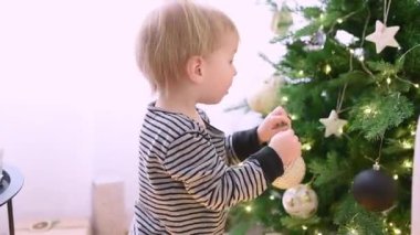 Genç bir çocuk güzel aydınlatılmış bir Noel ağacını ışıldayan süslemelerle süslüyor. Yeni yürümeye başlayan çocuk meşgul ve meraklı. İçerideki bayram ruhunun tadını çıkarıyor..