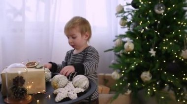 Genç bir çocuk güzel aydınlatılmış bir Noel ağacını ışıldayan süslemelerle süslüyor. Yeni yürümeye başlayan çocuk meşgul ve meraklı. İçerideki bayram ruhunun tadını çıkarıyor..